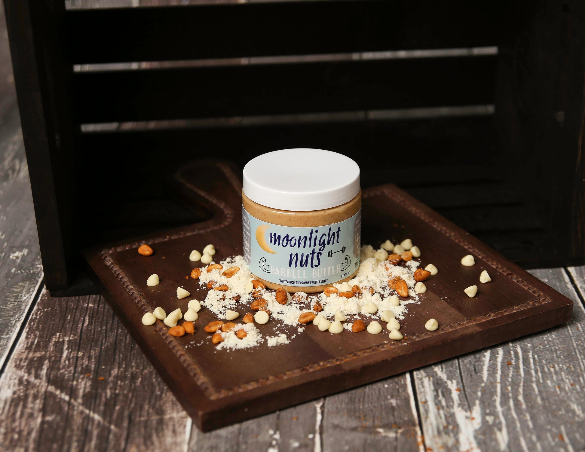 Jar of 'moonlight nuts barbell butter’ protein peanut butter on a wooden surface with scattered ingredients
