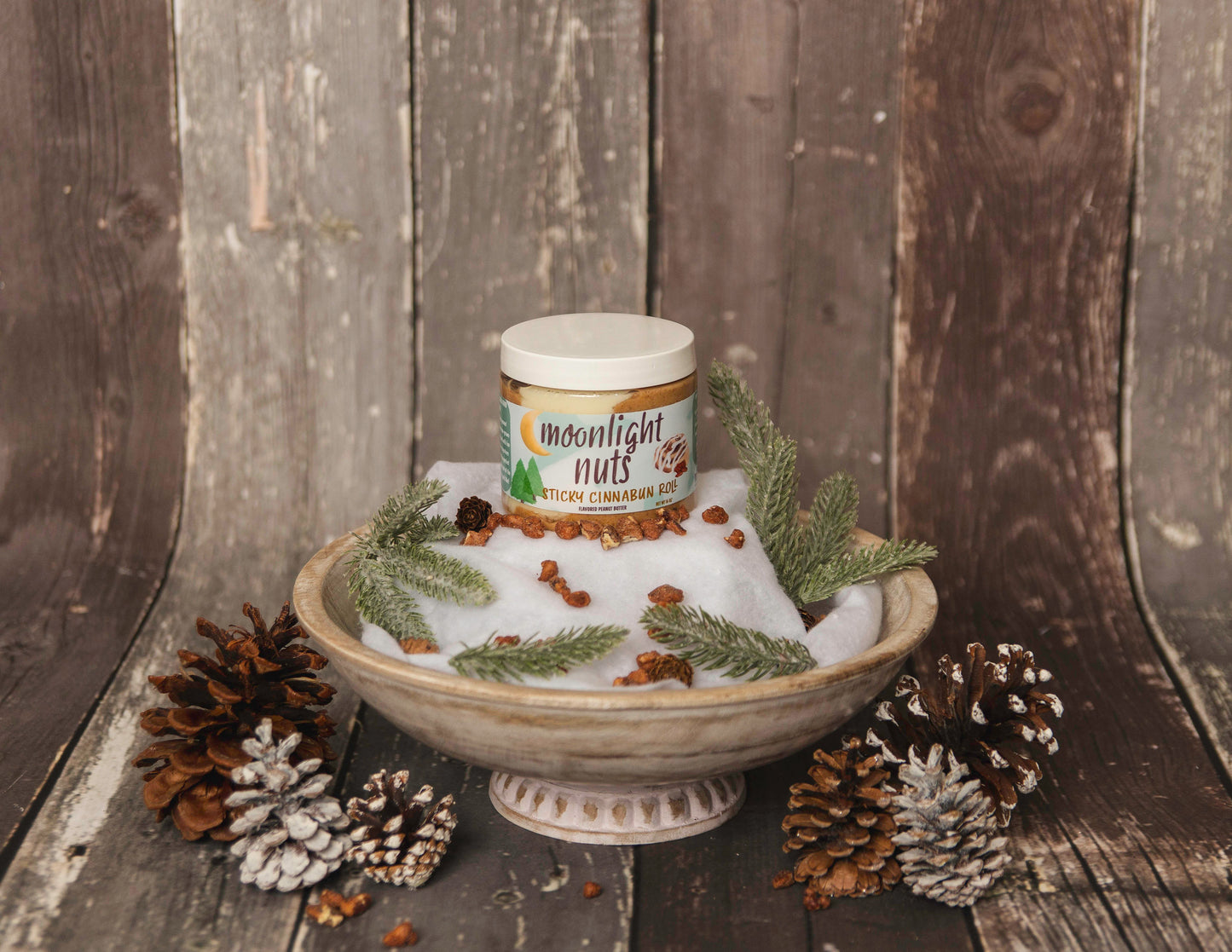 Jar of 'Moonlight Nuts' on a decorative stand with pine cones and greenery against a wooden background