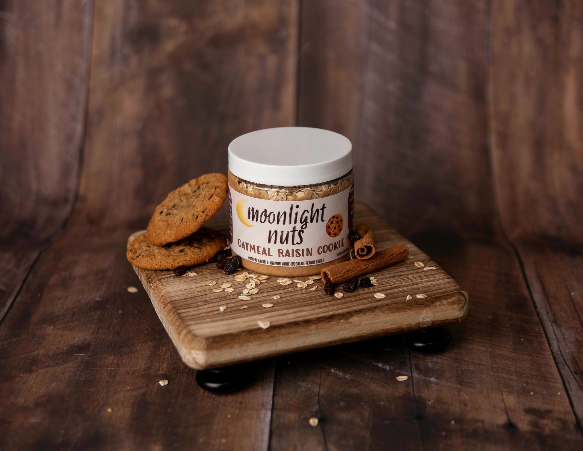 Jar of Moonlight Nuts gourmet peanut butter on a wooden tray with cookies and cinnamon sticks against a wooden background