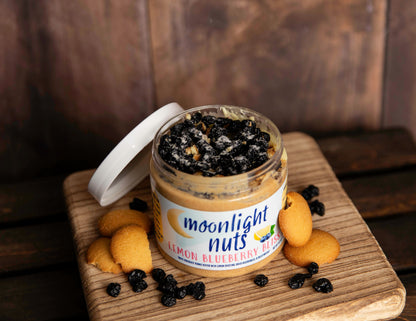 Open jar of Lemon Blueberry Bliss peanut butter showing chopped nilla wafers, dried blueberries, and lemon crystals on top of white chocolate peanut butter