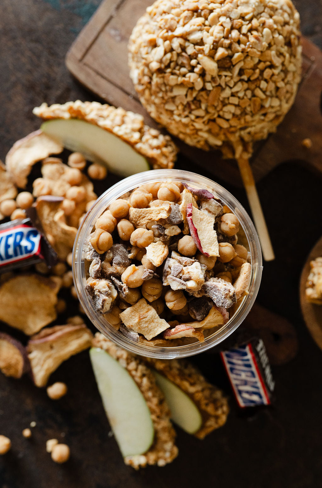 Top view showing all the toppings(freeze dried apples, apple chips, snickers, and caramel bits) of moonlight nuts caramel apple snickers peanut butter
