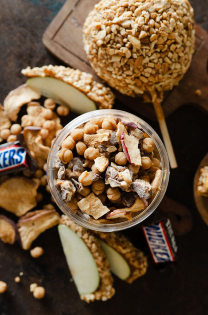 Top view showing all the toppings(freeze dried apples, apple chips, snickers, and caramel bits) of moonlight nuts caramel apple snickers peanut butter
