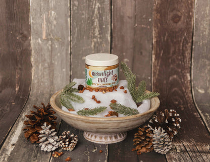 Jar of 'Moonlight Nuts' on a decorative stand with pine cones and greenery against a wooden background